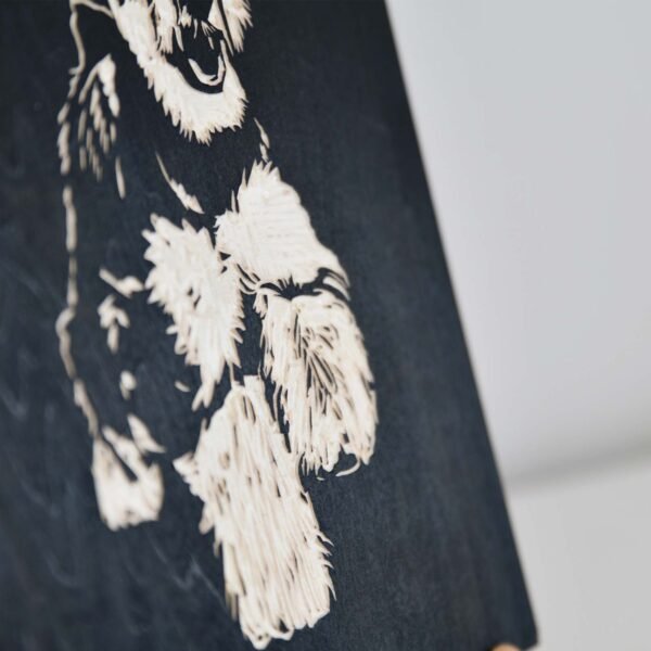 This Custom Wooden Engraved Pet Portrait is a handmade, eco-friendly memorial gift that beautifully captures a fluffy dog's face and front paws in detailed black and white engraving. Expertly carved into a dark wooden surface, this portrait features an out-of-focus background that highlights the texture and intricate details of the engraving.