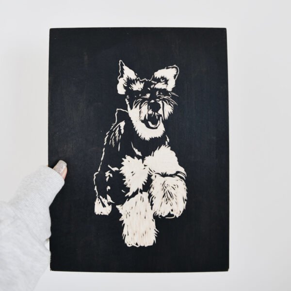 A person is holding a Custom Wooden Engraved Pet Portrait, a beautifully handmade and eco-friendly memorial gift, featuring a detailed light-colored depiction of a playful, fluffy dog with large ears and an open mouth set against a dark background.